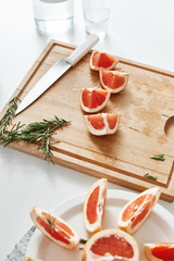 Close up of grapefruit pieces knife and rosemary on wooden desk. Copy space.