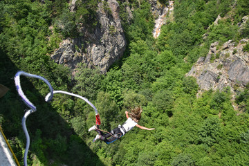 Bungee jumper girl with winded hair falling down from a 230-feet height bridge, rocks and green trees seen at the background