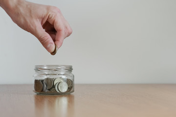 Hand putting money coin in to the glass jar