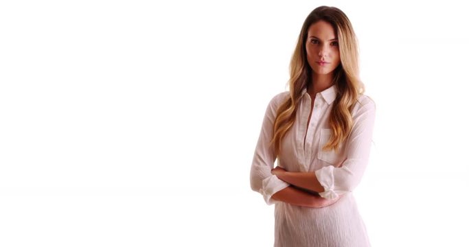 Young woman standing with arms crossed looking at camera with serious expression on white background with copyspace. Portrait of millennial in button down looking confidently at camera in studio. 4k 