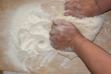 Top view shot of female hands mixing dough. Female hands knead dough on wooden board.