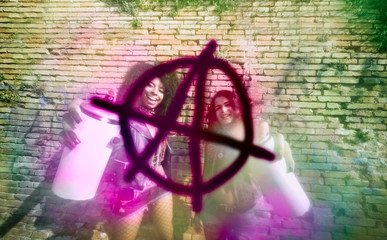 punk girls spray on wall. multi-racial teenage girls with color spray drawing anarchy symbol on a...