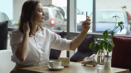 Obraz premium Young beautiful girl doing selfie on camera smartphone sitting in cozy cafe
