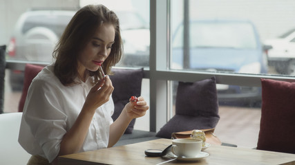 Business woman refreshing make-up after lunch break in cafe. girl paints lips