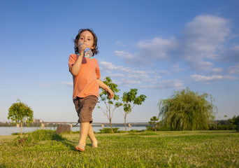 child with a bottle running along the grass.