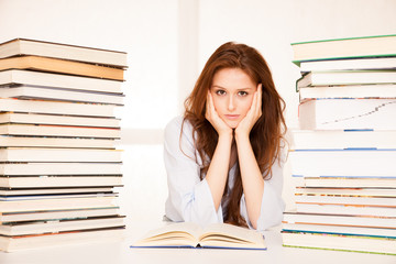 attractive young woman studies wtih hugr book piles on her desk