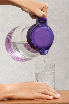 hands pouring water into a glass from a jug