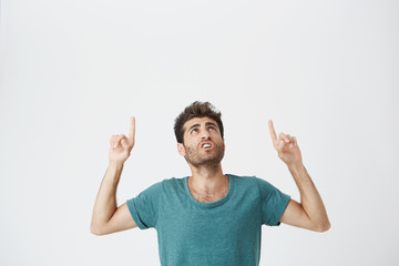 Young amazed stylish man with beard pointing his fingers at white background with copy space for your advertisement or promotional information.