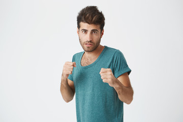 Strong, resolute man in blue t-shirt with beard standing in a fighting stance on a white...