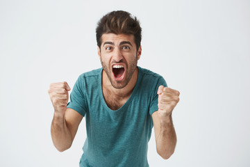 Emotions and achievement concept. Close up shot of happy successful casually weared student or employee screaming with winning expression, fists pumped, celebrating success on a white background.
