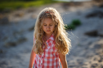 Little blonde child girl walking in summer beach at sunset.