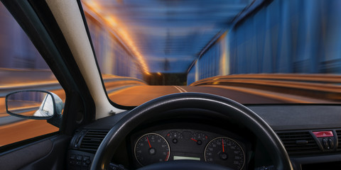 A view of the cockpit of a car driving at night through an illuminated bridge