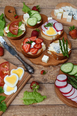 Set of healthy whole wheat bread sandwiches with fuits, vegetables, cheese and leafy green herbs on picnic wooden table. Ciabatta sandwich bar or buffet. Top view. Making lunch time snacks concept