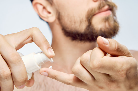 A young guy with a beard on a light background applies a cosmetic cream