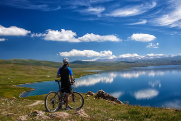 A young man with a bicycle on the background of the high mountain lake Song Kol