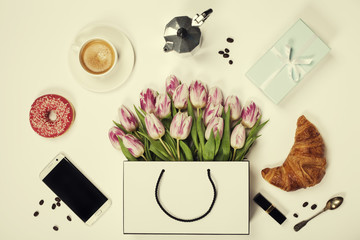 Top view of spring flowers, coffee, mobile phone, croissants, gift and cosmetics