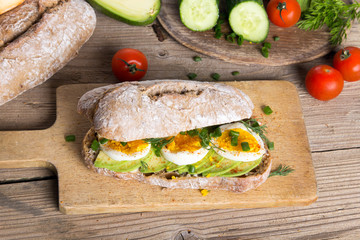Avocado and egg sandwich on a wooden background. Fresh organic vegetables, eggs and whole wheat bread. Healthy breakfast. Rustic style.
