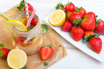 Mineral  water with fresh strawberries, lemon  and mint in jar on a white wooden background, copy space