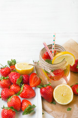 Mineral  water with fresh strawberries, lemon  and mint in jar on a white wooden background, copy space