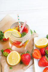 Mineral  water with fresh strawberries, lemon  and mint in jar on a white wooden background, copy space