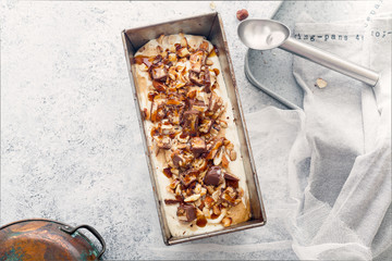 Snickers ice cream with caramel,  fried peanuts and hazelnuts in metallic baking tray on rustic background. Gourmet summer treat concept. Composition with copy space.