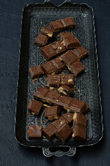 Milk chocolate with nuts and dried fruits on a metal tray on a dark concrete background