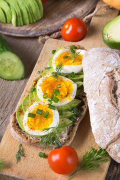 Avocado and egg sandwich on a wooden background. Fresh organic vegetables, eggs and whole wheat bread. Healthy breakfast. Rustic style.