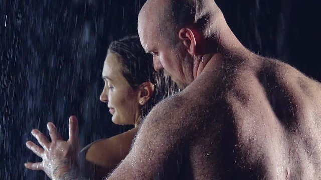 Nude man with a muscular hairy back touches his beloved woman pressed against her back with his chest. he's bald and brutal. in the darkness under the shower.