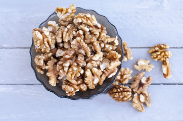 Many walnut kernels in a glass bowl on a wooden background of a gray-blue color.