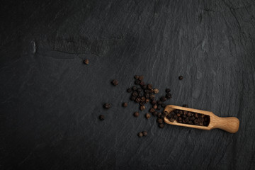 Fototapeta na wymiar Seeds of pepper scattered on a stone black background.