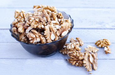 Many walnut kernels in a glass bowl on a wooden background of a gray-blue color.