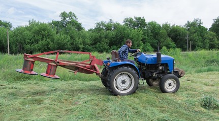 Fototapeta premium A man on a tractor mowing hay, mower lifted into transport position