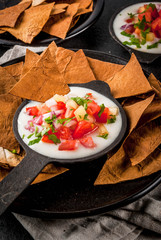 Mexican, LatinAmerican cuisine. Queso blanco recipe - cream cheese, cream, fresh stewed vegetables tomatoes, onions, peppers,  herbs. With Baked Tortilla Chips, black stone table.  copy space