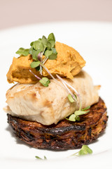 Delicious white fish served on fried zuchini, with sweet potato mash and purple sauce, white plate,  light brown background