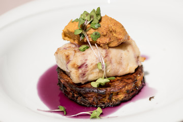 Delicious white fish served on fried zuchini, with sweet potato mash and purple sauce, white plate,  light brown background