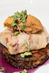 Delicious white fish served on fried zuchini, with sweet potato mash and purple sauce, white plate,  light brown background