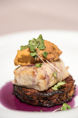 Delicious white fish served on fried zuchini, with sweet potato mash and purple sauce, white plate,  light brown background