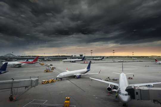 Vehicles And Ariplane Parking In Airport Ramp In Cloudy Sky