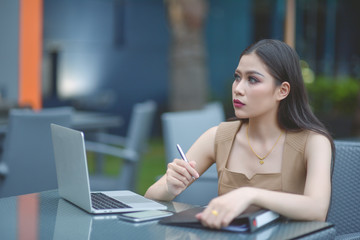 Sharing good business news. Attractive young woman talking on the mobile phone and smiling while sitting at her working place in office and looking at laptop, businesswoman working. Selective focus.