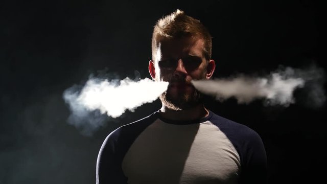 Guy smokes an electronic cigarette, enjoy the moment. Black background