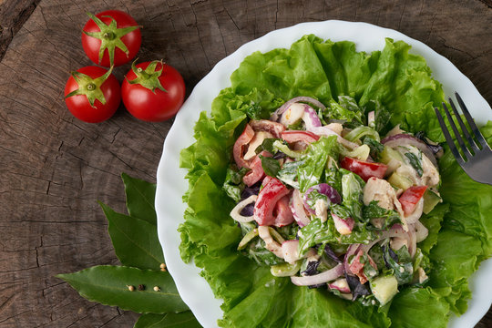 Fresh salad with fresh red cerry tomatoes, cucumbers, chicken, red onion, radish, bell pepper, lettuce with special spisy sauce on wooden table. Healthy eating and diet concept.