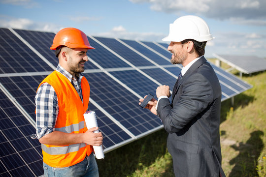 Business client showing photovoltaic detail to foreman. Solar energy station in the field, worker ond order comminicating.