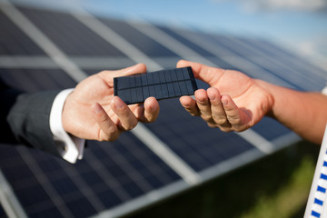 Close up view of photovoltaic item, solar panel in backstage. Hands of two men holding photovoltaic detail.