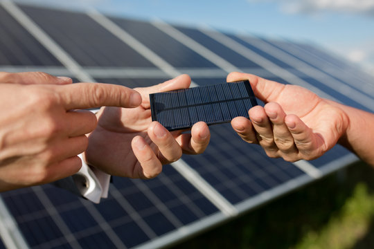 Solar energy, two hands holding photovoltaic item. Solar panels in the field, close yp view on photovoltanic detail.