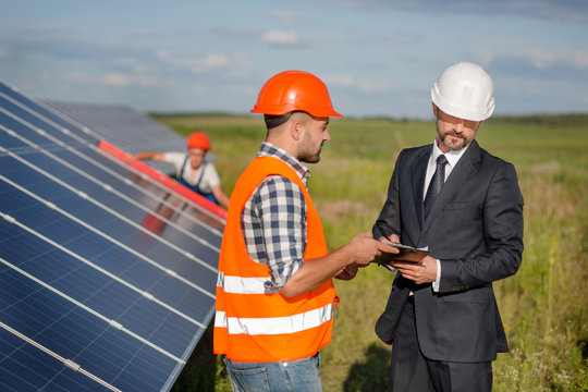 Businessman signing contract with foreman, technician examining solar panels at backdrop. Signing of agreement at solar energy station in the field.