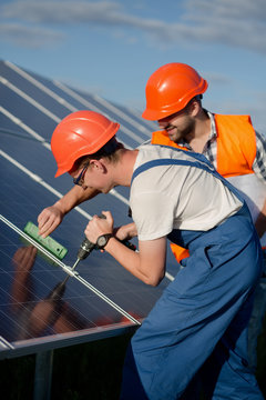 Technicians installing photovoltaic panels at solar power station. Workers checking solar panels equipment.