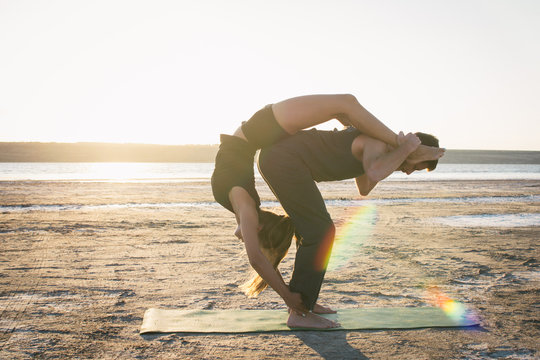 Young couple practicing yoga on beach at sunrise or sunset