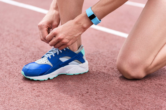 Legs of female runner adjusting shoelaces on running shoe
