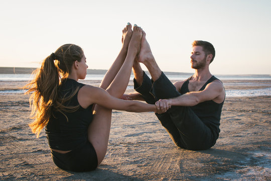 Young couple practicing yoga on beach at sunrise or sunset