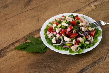 Summer fresh salad made of tomato, ruccola, chicken breast, arugula, crackers and spices and other different vegetables on wooden background